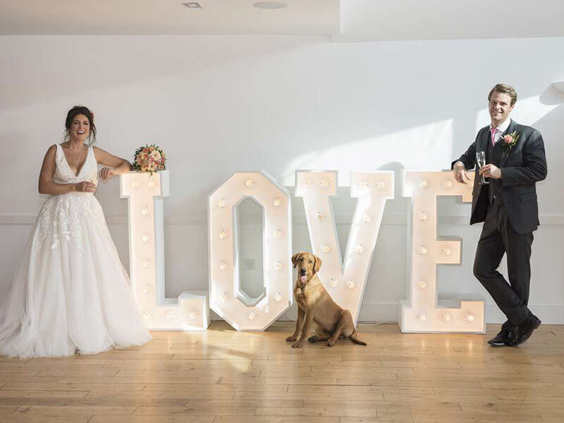 bride and groom in front of light up LOVE letters with dog