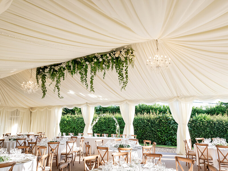the wedding breakfast set up in the marquee with floral ceiling arrangement