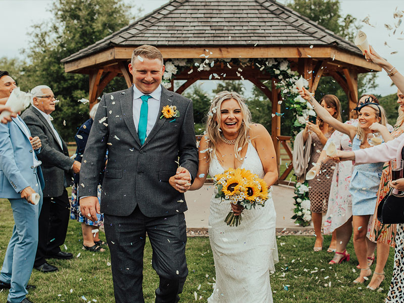 bride and groom with sunflower bouquet walking down the aisle with confetti